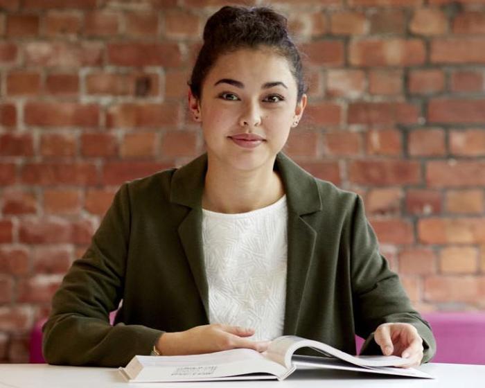 A student looking to camera in front of a brick wall